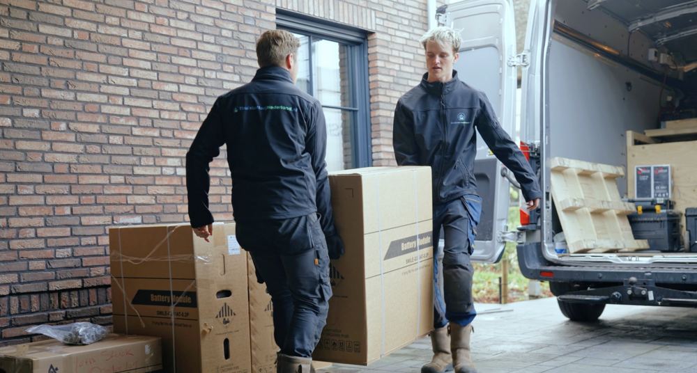 Twee monteurs van ThuisbatterijNederland.nl tillen een thuisbatterij uit de bus