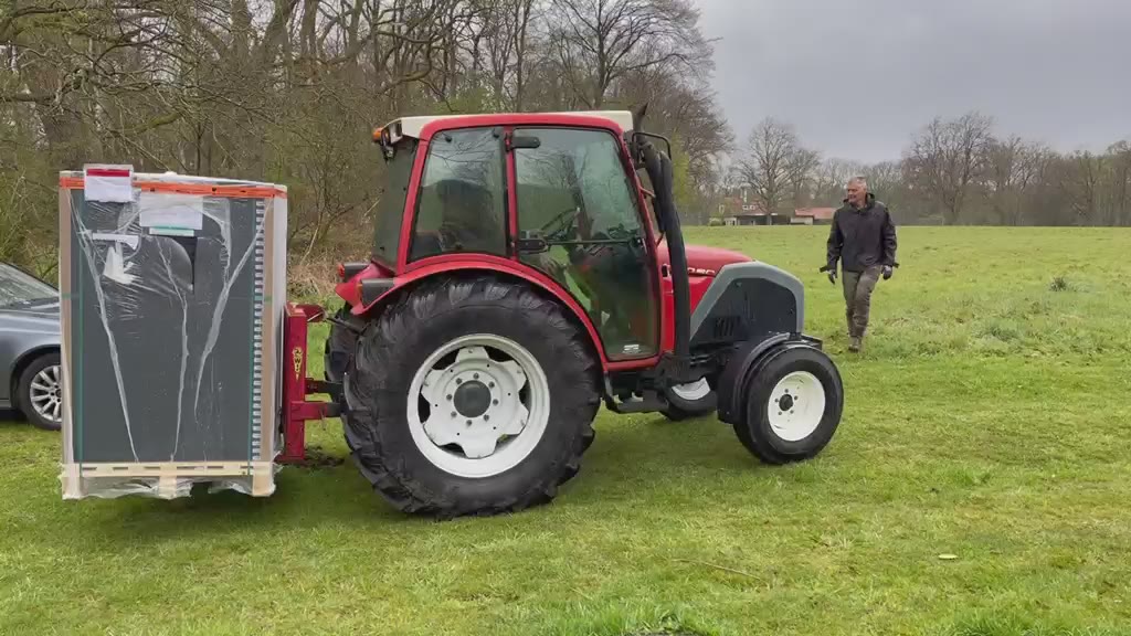 Een tractor rijdt een batterij het weiland op